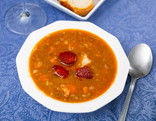 Portion of tratitional Spanish lentil soup with chorizo, sopa de lentejas, served on table.