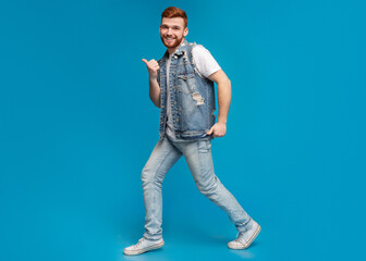 Fototapeta premium Cool millennial man dancing with thumbs up gestures on blue background, studio, copy space