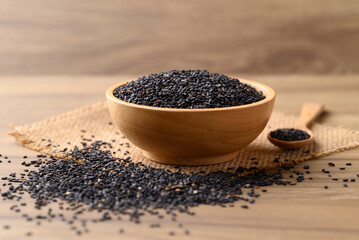 Black sesame seeds in bowl with spoon on wooden table, Food ingredient