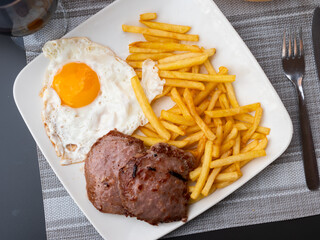 Spanish cuisine, roasted meat cutlet with fried potato and eggs on a white plate