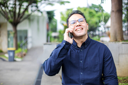 Cheerful Businessman Calling Using Mobile Phone While Walking on Park