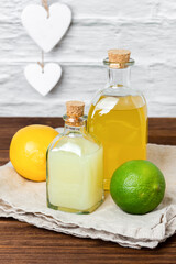 Lemon and lime syrups in glass bottle and fruits on wooden table.