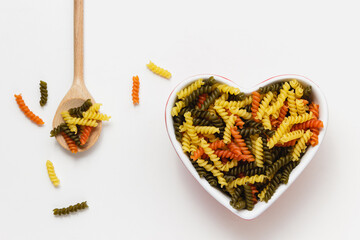 Raw fusilli in heart bowl on white background.