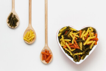 Raw fusilli in heart bowl on white background.