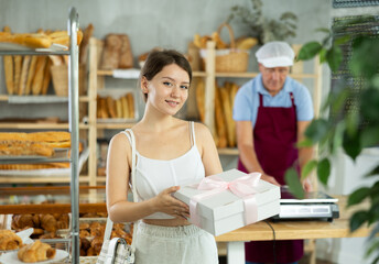 Portrait of young girl buyer with gift box of fresh baked goods in interior of a bakery