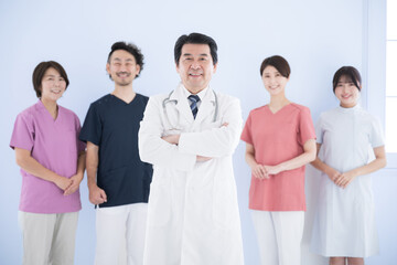 Obraz premium 横並びの医療従事者複数(5人)のイメージ ドクターと看護師、理学療法士チーム 腕を組むドクターの水色背景