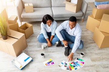 Home renovation concept. Young black couple choosing color palette for painting walls in new house,...