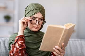 Senior Muslim Woman Having Poor Eyesight, Squinting Eyes While Reading Book Wearing Glasses At...