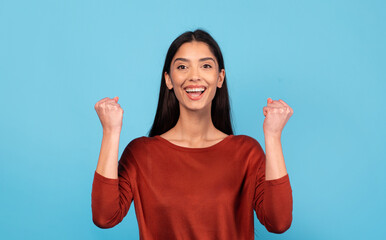 A young Middle Eastern woman is smiling brightly with her fists raised in celebration. She exudes...