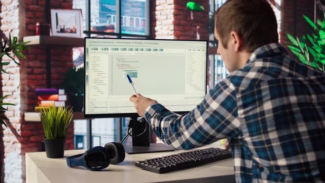 Programmer at desk types code into computer, developing software programs, entering commands. Man at home fixing errors in application, implementing new features pointing to code with pen, camera A