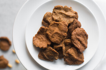 Overhead view of kuli-kuli on a white plate, top view of nigerian groundnut cakes on a plate, fresh homemade nigerian kulikuli on a ceramic plate