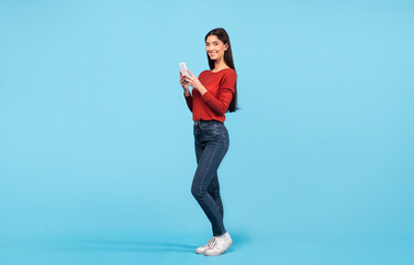 A young Middle Eastern woman stands on a bright blue background, smiling as she interacts with her...