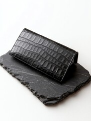 A sleek black wallet with a crocodile texture, resting on a dark slate surface, showcasing luxury and elegance in design.