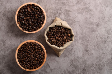 Roasted coffee beans in wooden bowl and sack isolated on dark cement background. Top view