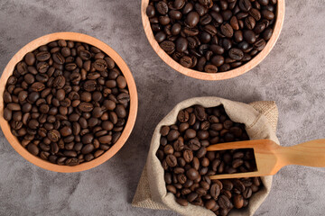 Roasted coffee beans in wooden bowl and sack isolated on dark cement background. Top view
