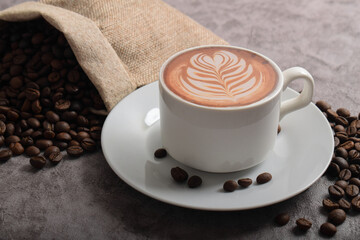 Cup of coffee latte with art shape and coffee beans on dark cement background.