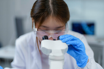 Asian female scientist adjusting microscope while working on medical research in laboratory