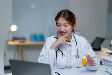 Young female doctor holding a medicine bottle while having a video consultation with a patient using her laptop in her office