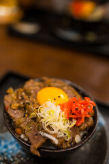 Roast Wagyu beef rice and raw egg bowl, the creamy yolk embrace the succulent beef, blending into a delectable harmony of textures and flavors in a black bowl.