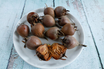 A close-up of medlar fruits displayed on a white plate, showcasing their unique texture and form. One fruit is cut open, revealing its soft, pulp-like interior and rich brown color.  .