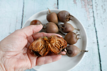 A close-up of medlar fruits resting in the palm of a hand, showcasing their unique texture and form. One fruit is cut open, revealing its soft, pulp-like interior and rich brown color.  