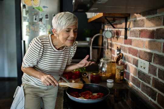 Senior woman cooking vegetables in modern kitchen and enjoying the aroma