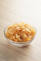 Cassava chips in a clear glass bowl on a plywood base photographed with studio light