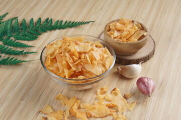 Cassava chips in a clear glass bowl on a plywood base photographed with studio light