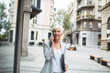 Senior businesswoman walking downtown using smartphone
