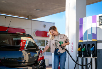 Attractive blonde in jeans and leather jacket filling up gas tank by herself 