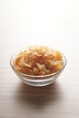 Cassava chips in a clear glass bowl on a plywood base photographed with studio light