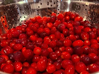 Bright red cranberries sit in a shiny metal colander, freshly washed, presenting vivid colors and natural textures, evoking thoughts of autumn, winter cooking, and festive celebrations.
