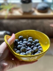 Freshly washed blueberries displayed in a vibrant yellow handheld berry colander, illuminated by natural sunlight, creating a warm and inviting kitchen scene with a healthy and delicious fruit snack.