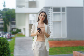 Young asian businesswoman walking confidently near an office building, using her smartphone to stay connected in a bustling urban environment