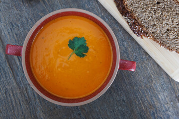 Freshly made tomato soup in a red ceramic bowl on a wooden dining table