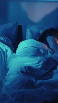 Vertical video. Gadget couple. Digital night. Social media addiction. Unhappy husband wife phubbing in bed using devices late in dark blue light.