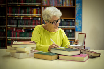Fototapeta premium Elder woman sitting enjoys reading book in quiet of the library appears focused and content books with the idea of self-growth and discovery at any stage of life.