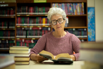 Elder woman sitting enjoys reading book in quiet of the library appears focused and content books...