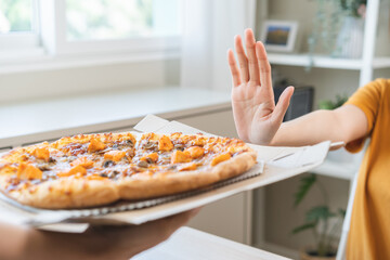 Diet concept, unhappy asian young woman, girl refusing to eat Pizza in box at home, hand pushing...