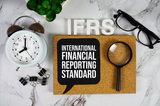 IFRS - International Financial Reporting Standard acronym with alarm clock and magnifying glass, business concept background