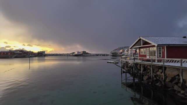 Scenic winter sunrise over calm waters in Lofoten, Norway, featuring cozy cabin