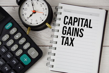 Capital Gains Tax text on notepad with alarm clock and calculator on wooden background