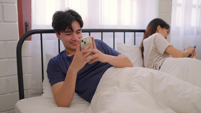 Asian man secretly chatting to mistress while lying in bed with girlfriend.