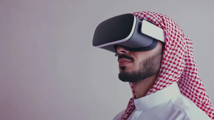 Arab man wearing a white thobe and red and white keffiyeh using a virtual reality headset.