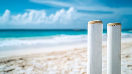 Close-up cricket wicket against beach horizon, pristine white stumps, wooden bails with detailed texture, azure sky, blurred waves backdrop, clean architectural composition, sports equipment detail