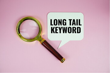 Long tail keyword text on speech bluble with magnifying glass top view on pink background