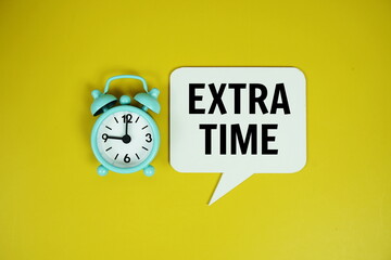 Extra time text on speech bluble with alarm clock top view on yellow background