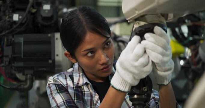 Professional female engineer wearing gloves and repairing robotic machinery in an industrial factory environment, showcasing precision engineering, advanced automation concept.