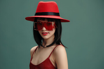Red hat, sunglasses, woman posing for the camera with hand on hip and the other in her hair,...