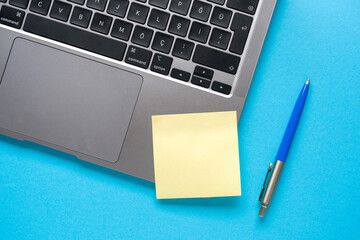 Top view of blank post-it stuck on laptop on blue table